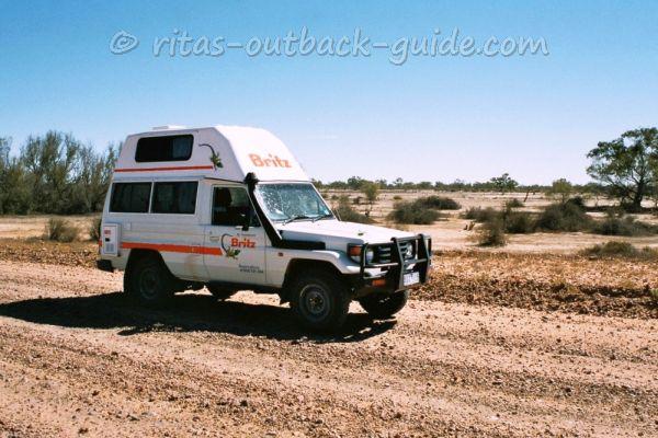 An outback campervan crossing the dry bed of Cooper Creek